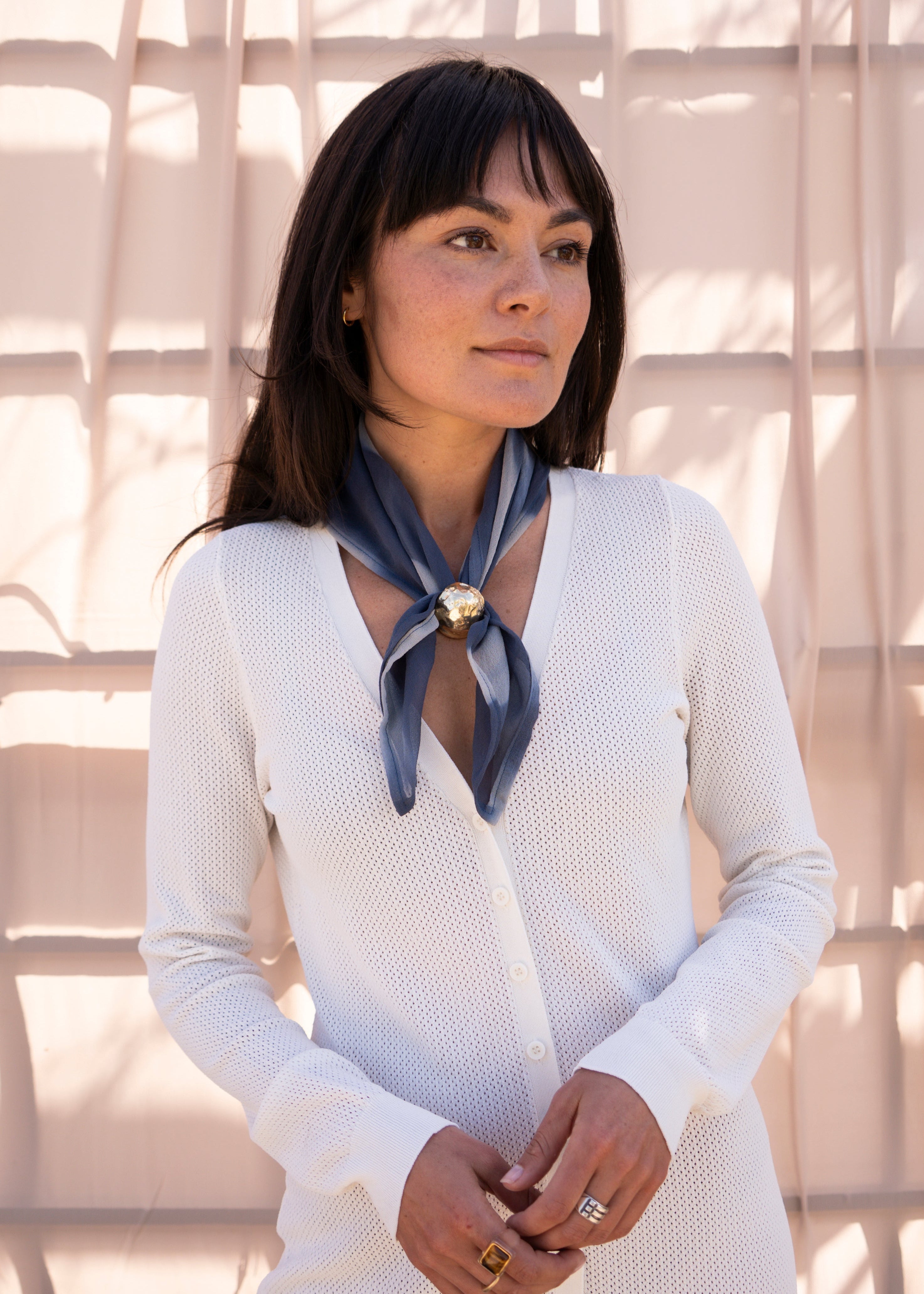 Woman wearing a white outfit with a blue scarf against a neutral background