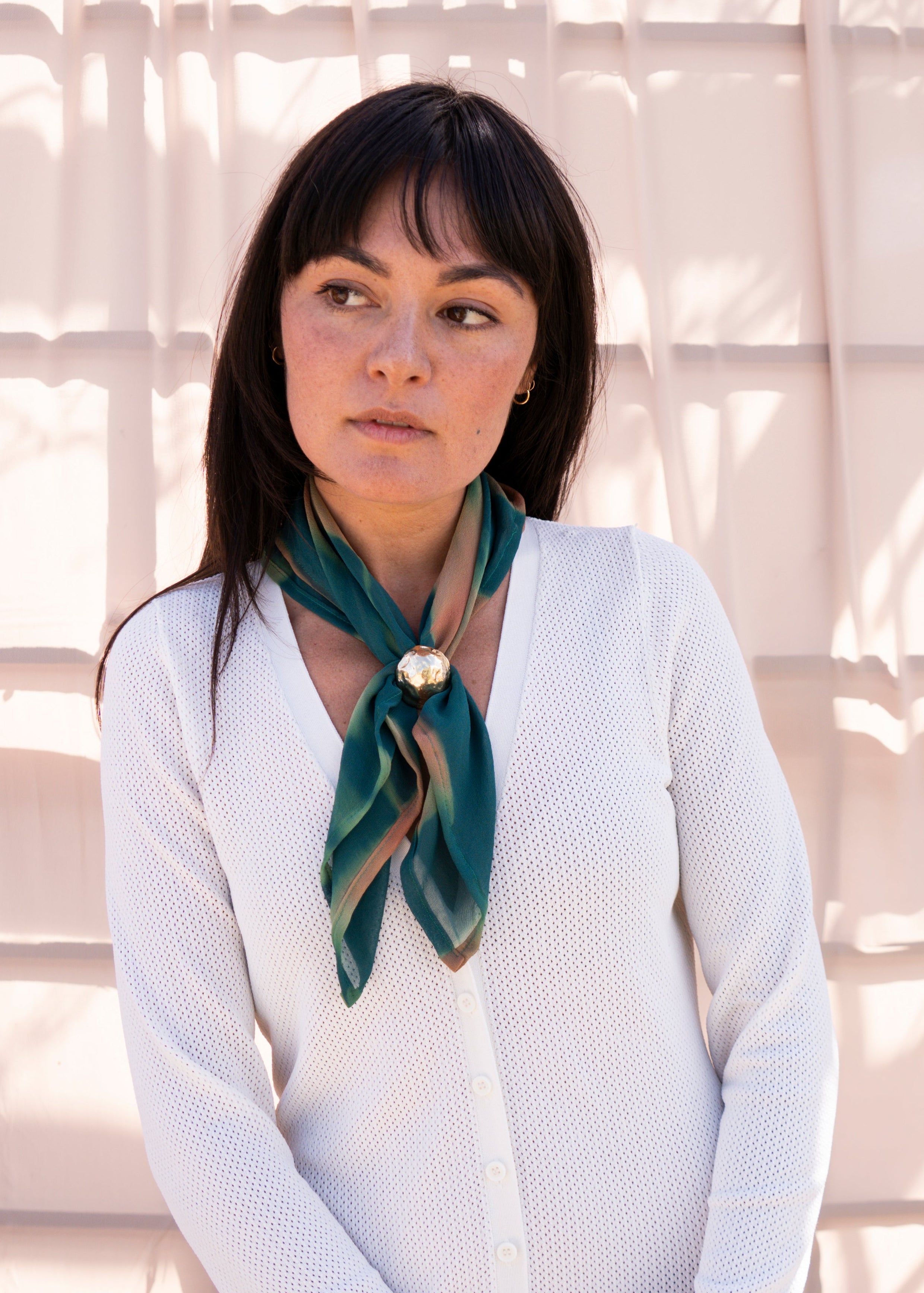 Woman wearing a white sweater and green scarf against a neutral background