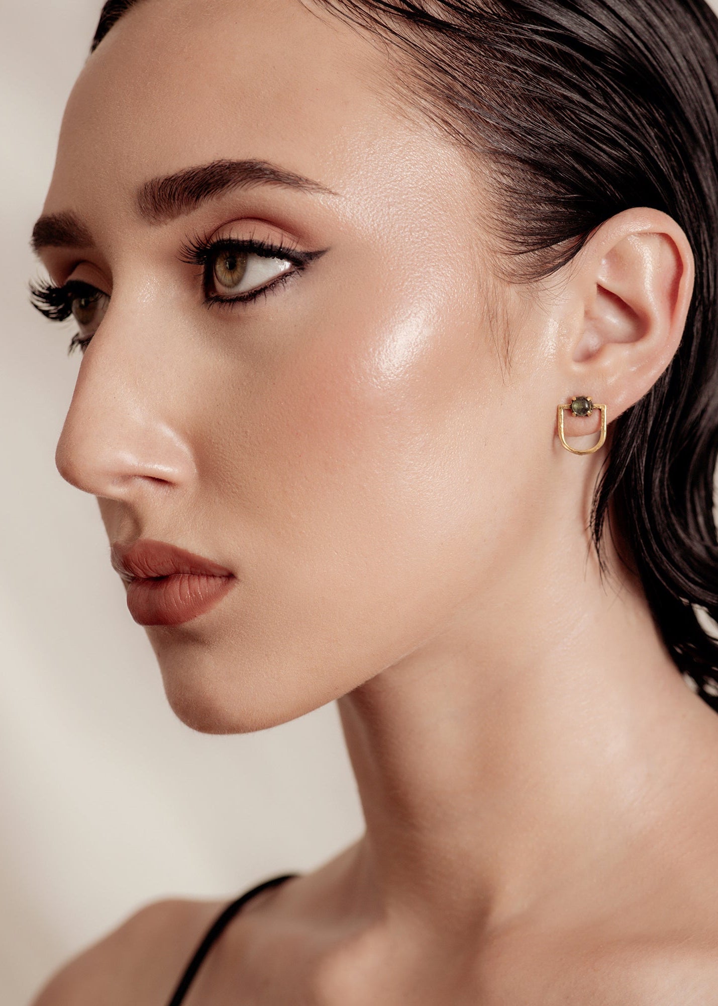 Woman wearing gold earrings with a neutral background