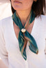 Person wearing a green scarf with a decorative brooch on a blurred background