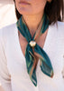 Person wearing a green scarf with a decorative brooch on a blurred background